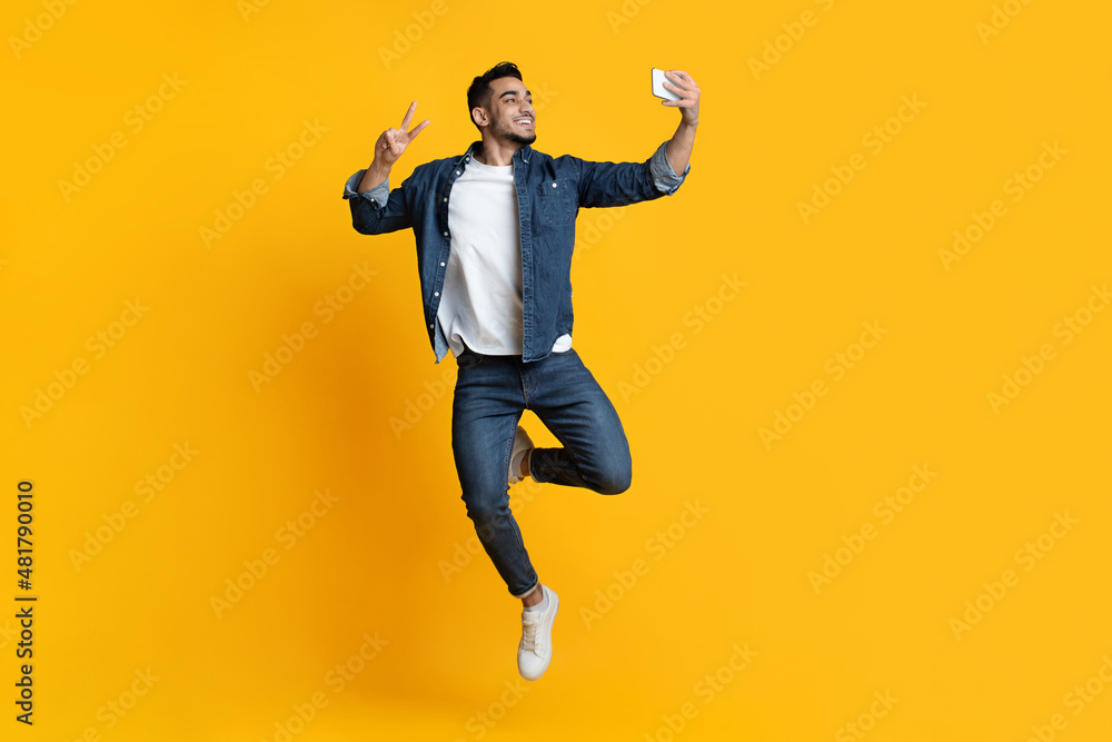 Cheerful handsome arab man taking selfie on yellow