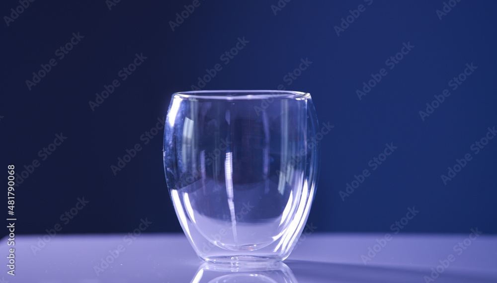 An empty transparent glass with double wall thermo resistant standing on a white table with dark background. An empty transparent glass with double wall thermo resistant standing on a white table with dark background.