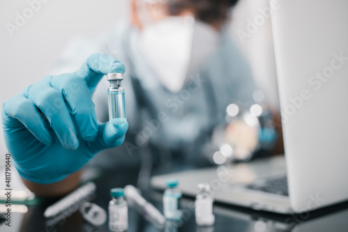 Fototapeta Naklejka Na Ścianę i Meble -  A doctor or scientist in the COVID-19 medical vaccine research and development laboratory holds a syringe with a liquid vaccine to study and analyze antibody samples for the patient.

