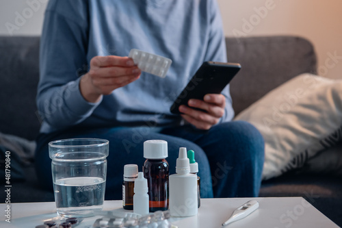 Medicine on the bedside table and woman checking information about pills in the Internet on the background. photo