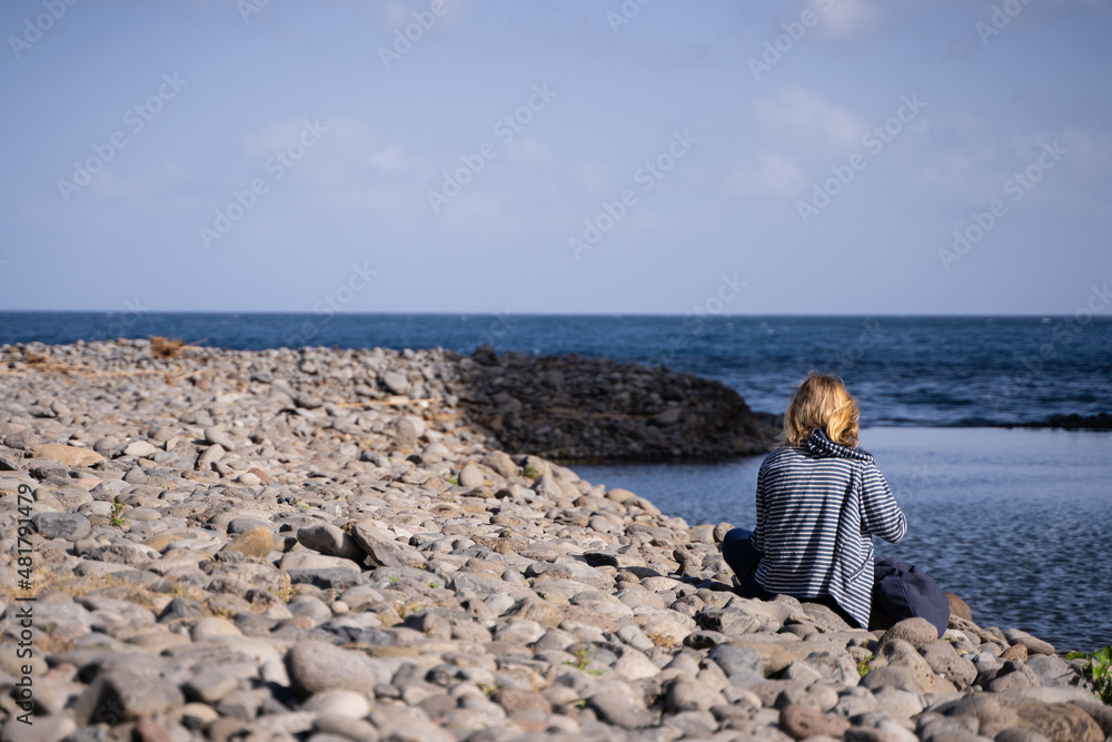 Young blonde woman sitting looking at the sea