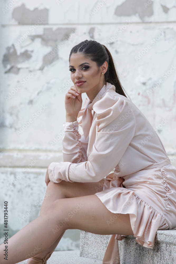 Outdoor portrait of gorgeous young woman with long ponytail in elegant satin dress
