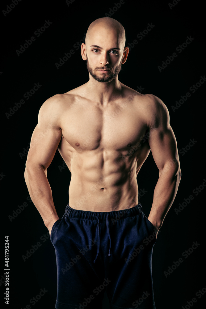 Athletic man with hands in pocket look straight at camera while show his well trained abs