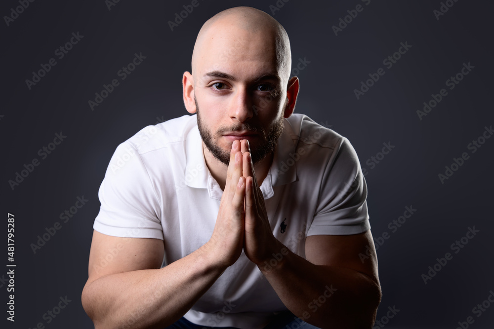 turkish man fold hands in front of his face like he is praying while look serious and neutral at camera isolated on grey