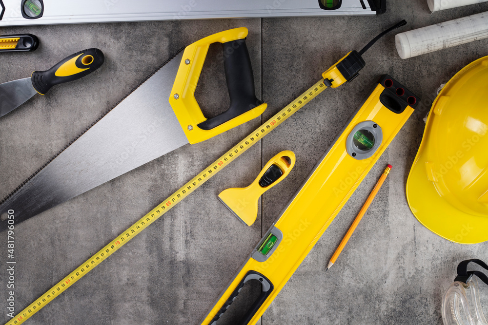 Contractor theme. Tool kit of the contractor: yellow hardhat, libella, hand saw. Plans and notebook on the desk.