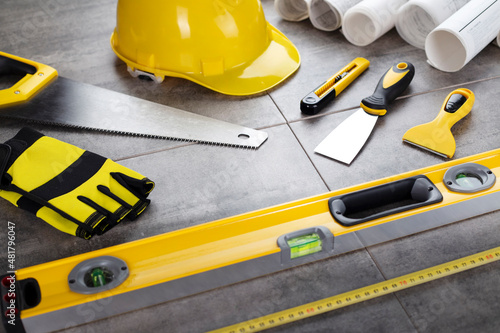 Contractor theme. Tool kit of the contractor: yellow hardhat, libella, hand saw. Plans and notebook on the desk.