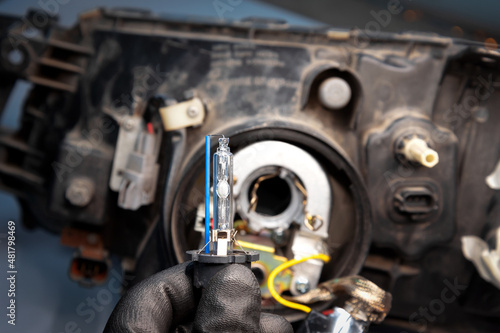 gloved hand holding a car lamp for replacement in a car headlight