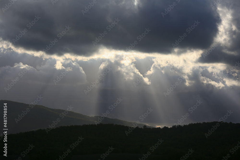 Beams of light from behind the clouds in the valley above the hills