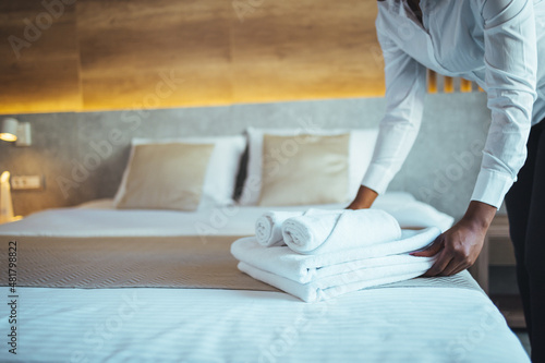 Quadro su tela Chambermaid in uniform holding stack of clean folded towels while going to put them on changed bed in hotel room