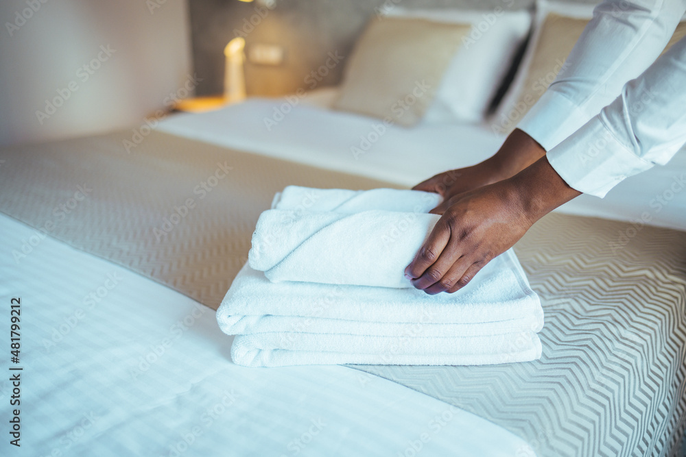 Young hotel maid making the bed with clean fresh towels. Hands of hotel maid bringing fresh towels to the room. Close up of a young hotel maid holding clean folded towels Young hotel maid making the bed with clean fresh towels. Hands of hotel maid bringing fresh towels to the room. Close up of a young hotel maid holding clean folded towels