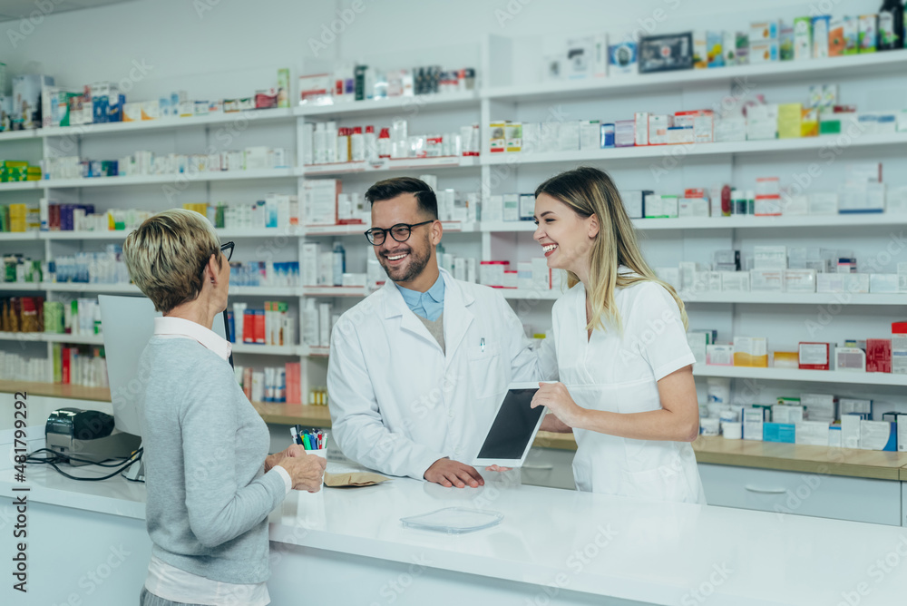 Fototapeta premium Two pharmacist giving prescription medications to senior female customer in a pharmacy