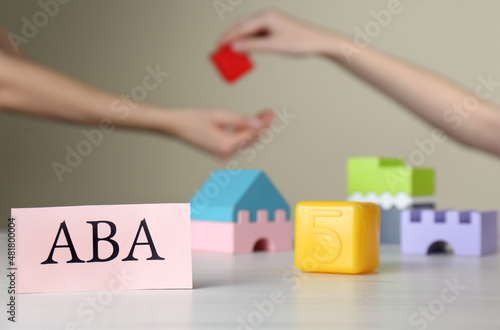 Paper card with abbreviation ABA (Applied behavior analysis) and blocks on white table, space for text