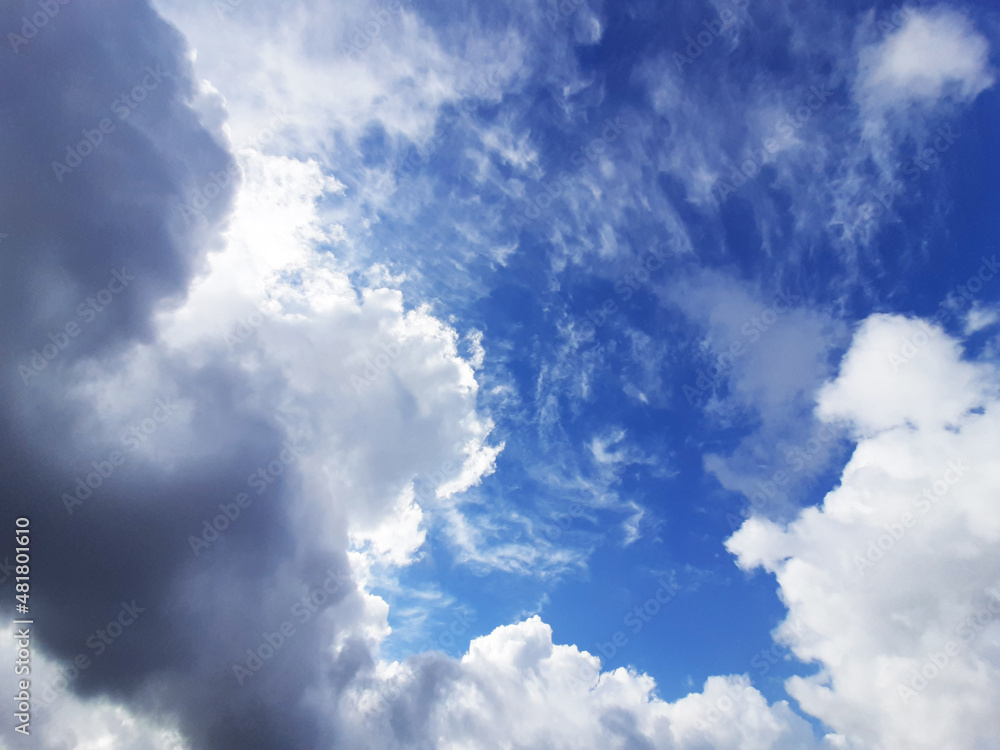 Lush clouds overhead in the sky block the sunlight. Through the layers of clouds, a blue sky peeks through. It's raining soon. Horizontal photo.