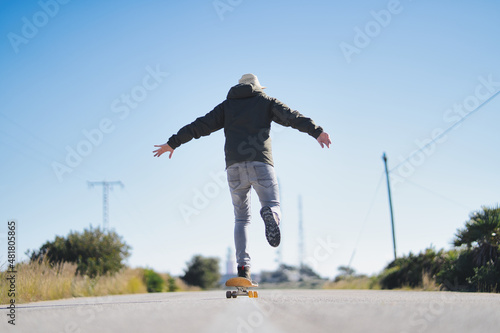 rear view of a young hipster on a skateboard, moving forward on a straight road. concept of happiness