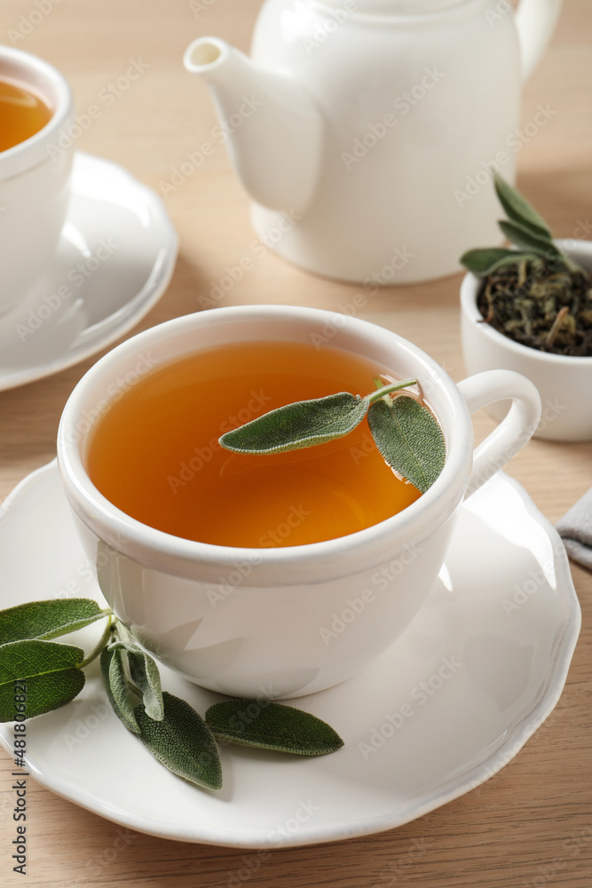 Cup of aromatic sage tea with fresh leaves on wooden table Cup of aromatic sage tea with fresh leaves on wooden table