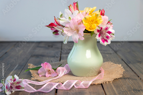 multi-colored blooming alstroemeria flowers in clay vase on wooden table with round napkin and a pink ribbon. the concept of summer  spring  nature bloom  holiday and congratulations. copy space.