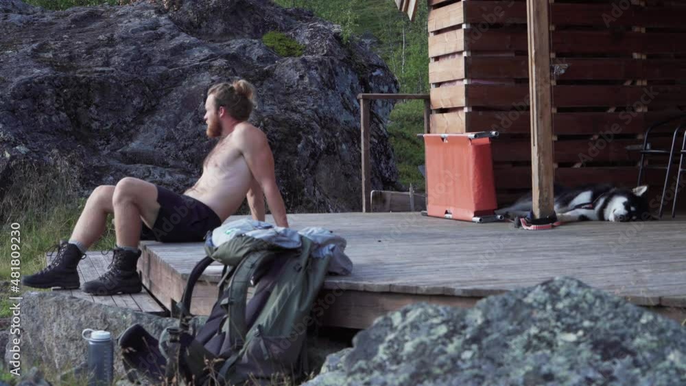 Norwegian Man Half Naked Looking Tired Resting On Wooden Porch Of A Cottage. Medium Shot Norwegian Man Half Naked Looking Tired Resting On Wooden Porch Of A Cottage. Medium Shot