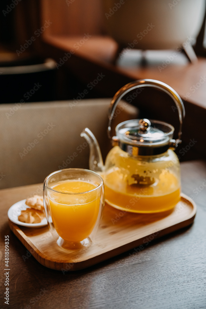 Pot and a glass with sea buckthorn tea served on a wooden tray at a cafe. Pot and a glass with sea buckthorn tea served on a wooden tray at a cafe.