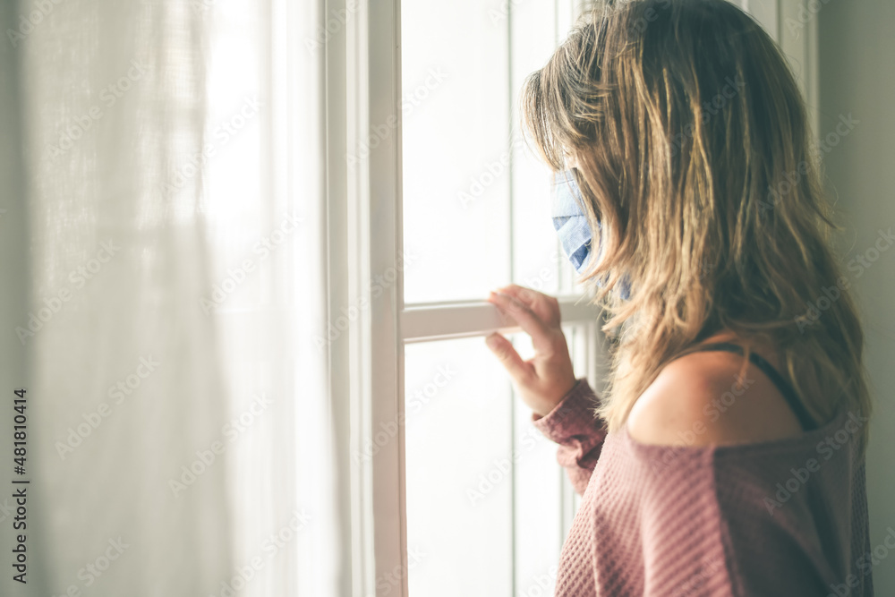 Young woman looking outside the window with surgical mask during coronavirus lockdown Virus covid-19 isolated people at home. Teen waiting to come back to the normal life Girl looks through the glass Young woman looking outside the window with surgical mask during coronavirus lockdown Virus covid-19 isolated people at home. Teen waiting to come back to the normal life Girl looks through the glass