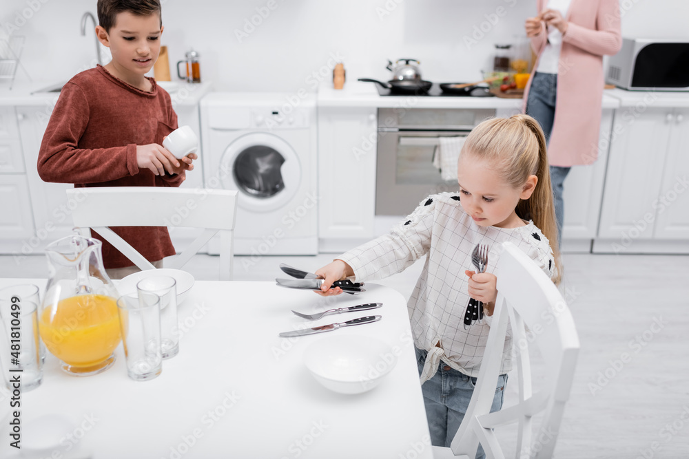 children setting table in kitchen while granny preparing breakfast. children setting table in kitchen while granny preparing breakfast.