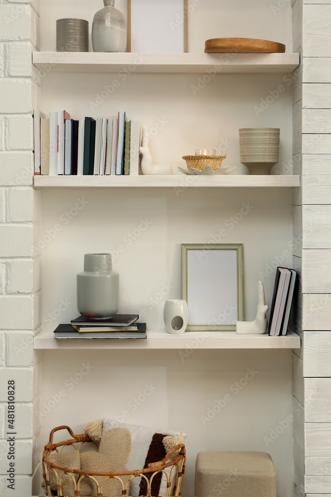 Fototapeta premium Books, empty frames and different decor on shelves indoors. Interior design