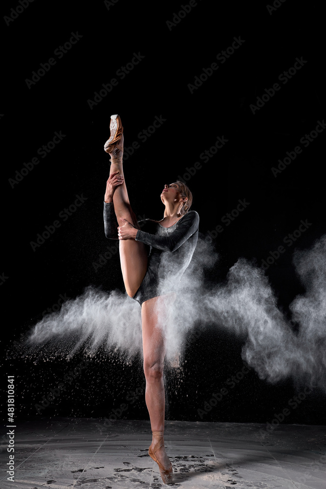 Dancing in flour concept. Young beautiful female adult woman dancer in dust, fog. Lady is wearing black bodysuit, making dance element in flour cloud on isolated black background