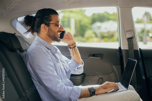 Positive arab man freelancer working online while sitting in taxi