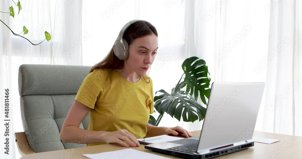 Lovely young woman putting on headphones while sitting on chair at desk at home Lovely young woman putting on headphones while sitting on chair at desk at home