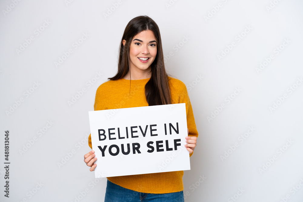 Young Brazilian woman isolated on white background holding a placard with text Believe In Your Self with happy expression Young Brazilian woman isolated on white background holding a placard with text Believe In Your Self with happy expression