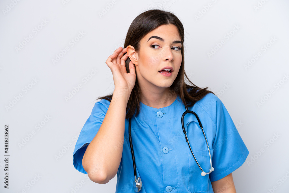 Young Brazilian nurse woman isolated on white background listening to something by putting hand on the ear Young Brazilian nurse woman isolated on white background listening to something by putting hand on the ear