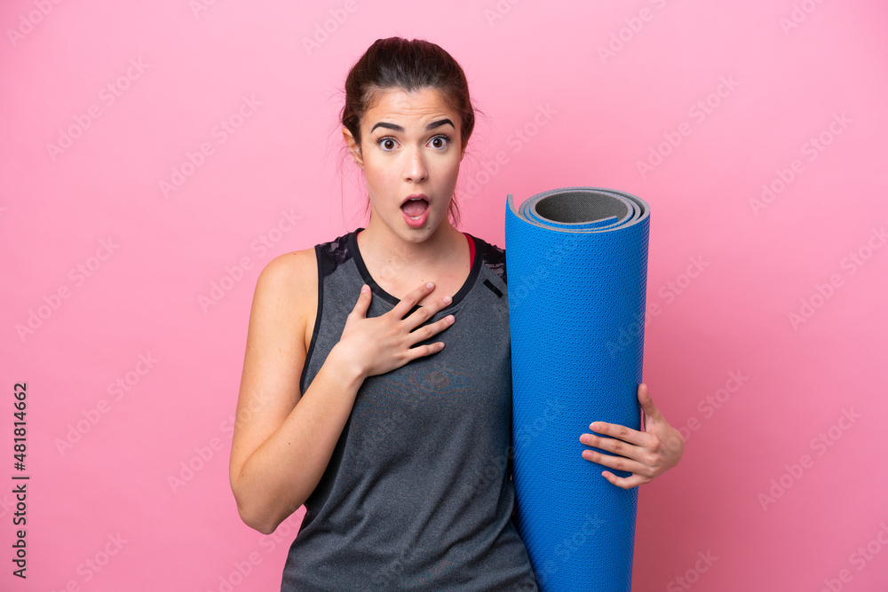 Young Brazilian sport woman going to yoga classes while holding a mat isolated on pink background surprised and shocked while looking right Young Brazilian sport woman going to yoga classes while holding a mat isolated on pink background surprised and shocked while looking right