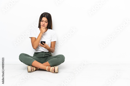 Teenager girl sitting on the floor thinking and sending a message