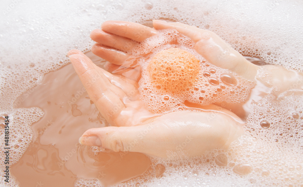 Fototapeta premium A girl in a white bathroom with foam dissolves a bright bath bomb in water