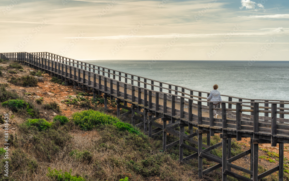 woman walking on a wooden walkway over the cliff in Alvor, Algarve, Portugal
