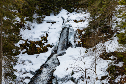 Long high waterfall in mountains full of snow and ice around