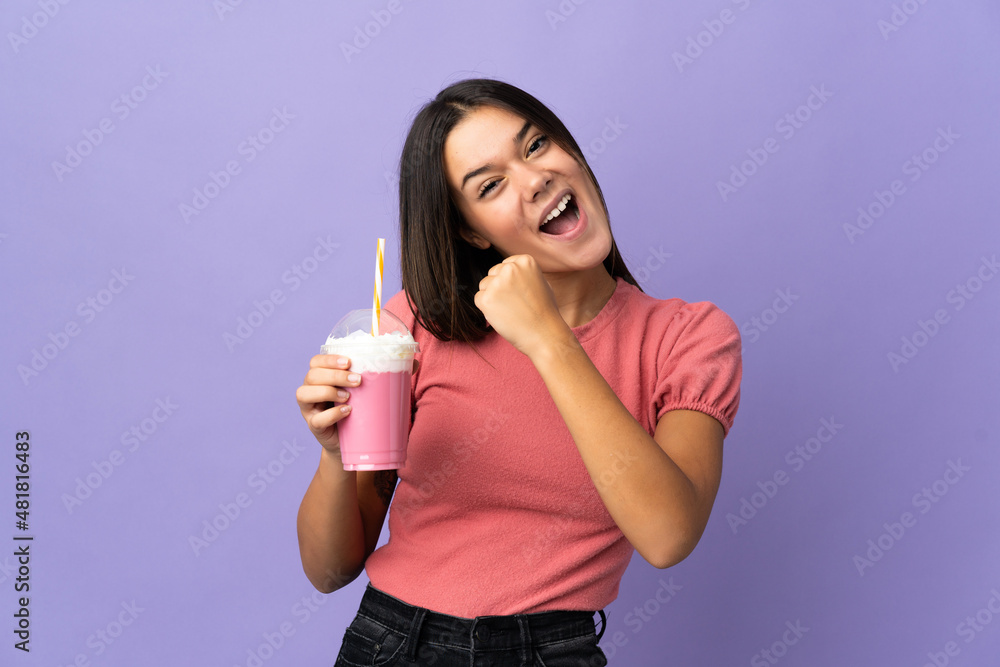 Teenager girl holding a strawberry milkshake celebrating a victory Teenager girl holding a strawberry milkshake celebrating a victory