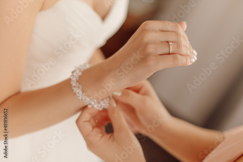 Crop photo of hands of unrecognisable woman preparing bride for wedding day helping to fasten bracelet on her hand.