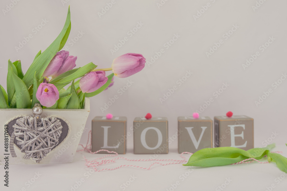 Fototapeta premium Walentynkowe tło, różowe tulipany w pudełku drewnianym z serduszkiem i napis z brył drewnianych układające się w sowo love.