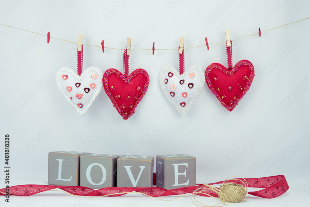 Walentynkowe tło, wiszące białe i czerwone serca i napis z drewnianych brył z liter tworzące słowo love. - obrazy, fototapety, plakaty 