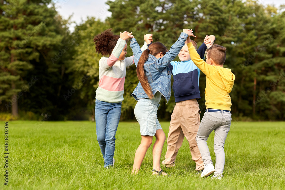 Fototapeta premium childhood, leisure and people concept - group of happy kids playing round dance at park