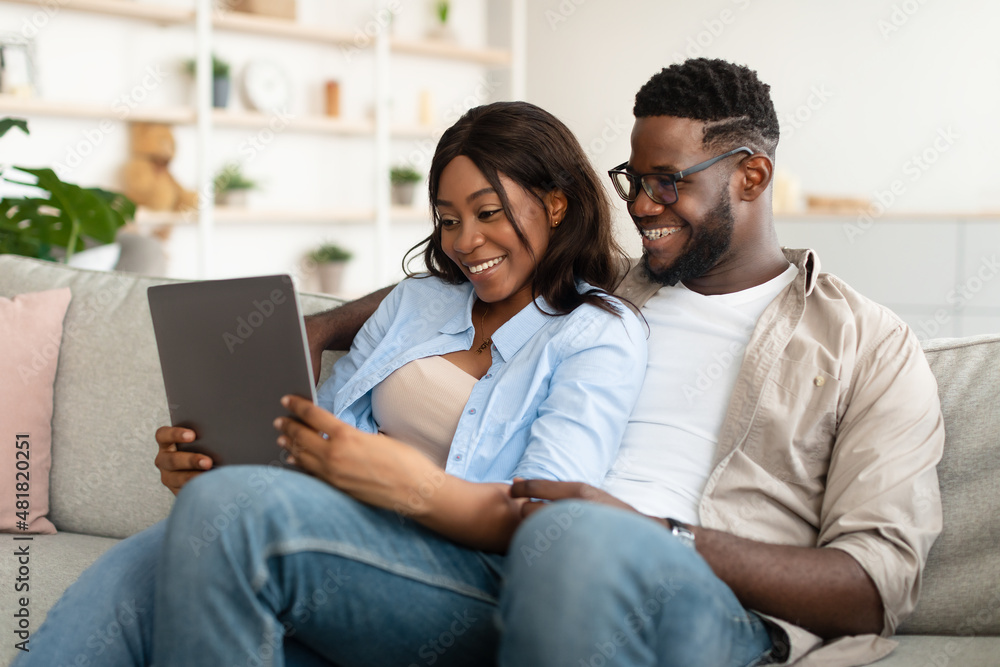 African american couple sitting on couch, using tablet African american couple sitting on couch, using tablet