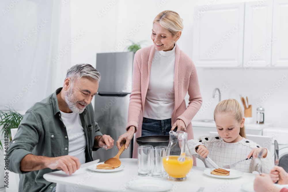 happy woman serving pancakes for husband during breakfast with grandchildren. happy woman serving pancakes for husband during breakfast with grandchildren.