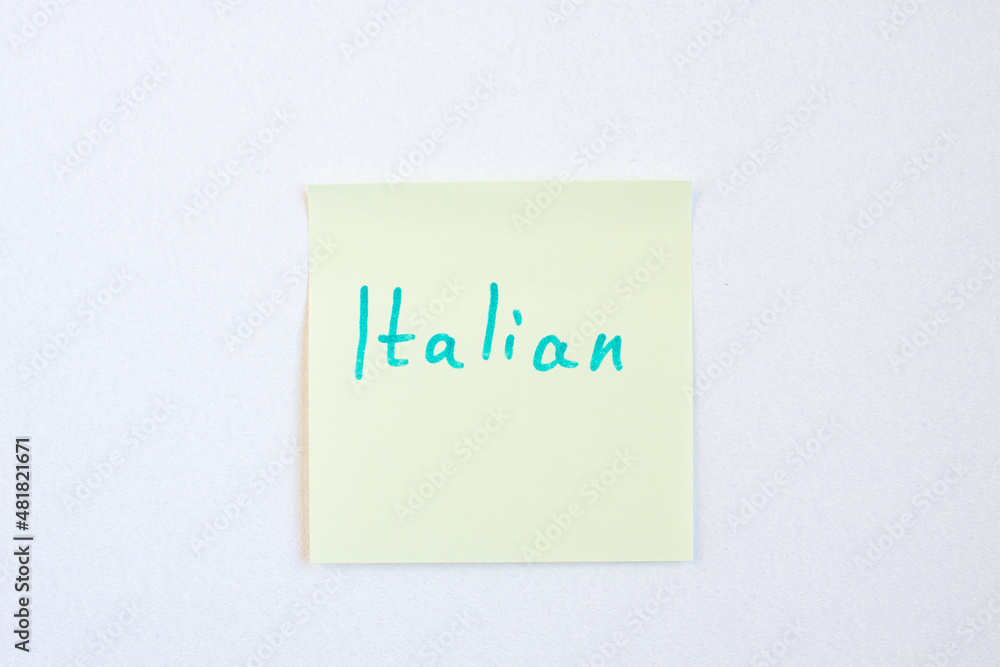 Top view flat lay of the reminder notepaper of yellow color with word Italian on it on white background. Flashcards and language studies concept Top view flat lay of the reminder notepaper of yellow color with word Italian on it on white background. Flashcards and language studies concept