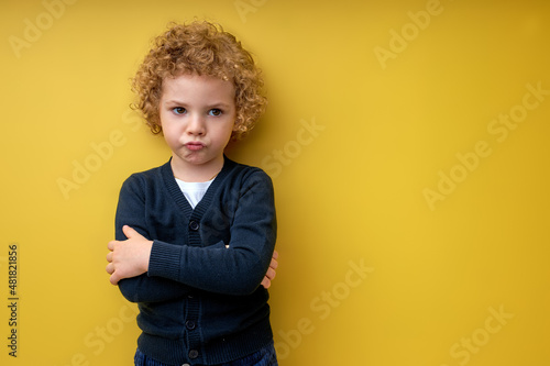 Tableau sur toile Resentful sad child boy stand with arms folded posing isolated on yellow studio background
