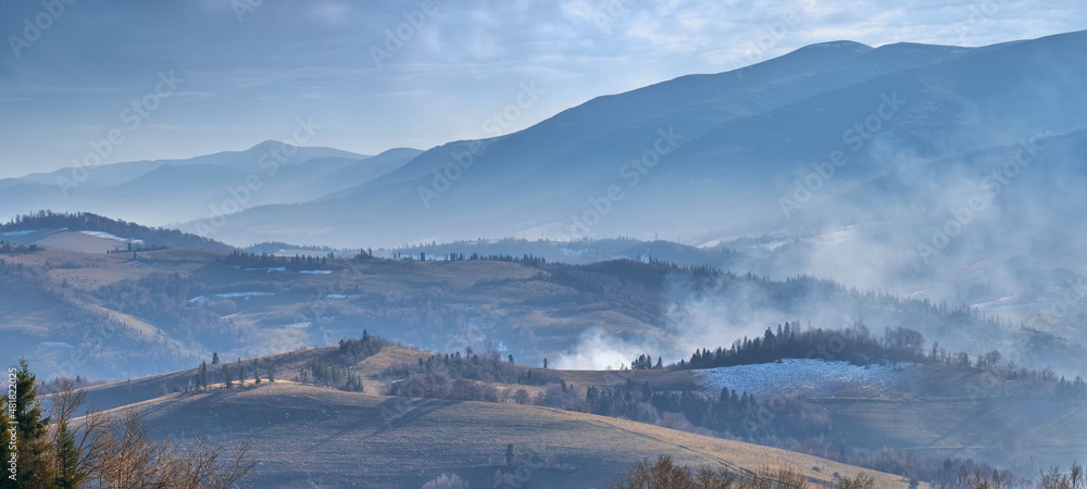 The beginning of winter in the Carpathian mountains. Cold blue gamma, trees without leaves, withered grass. Fires are lit in the villages