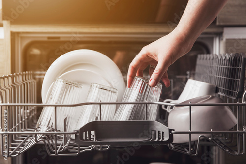 Female hand loading dished, empty out or unloading dishwasher with utensils. Kitchen appliances, lifestyle view. Woman puts a plate in the dishwasher or takes from it. Housewife does her housework  photo