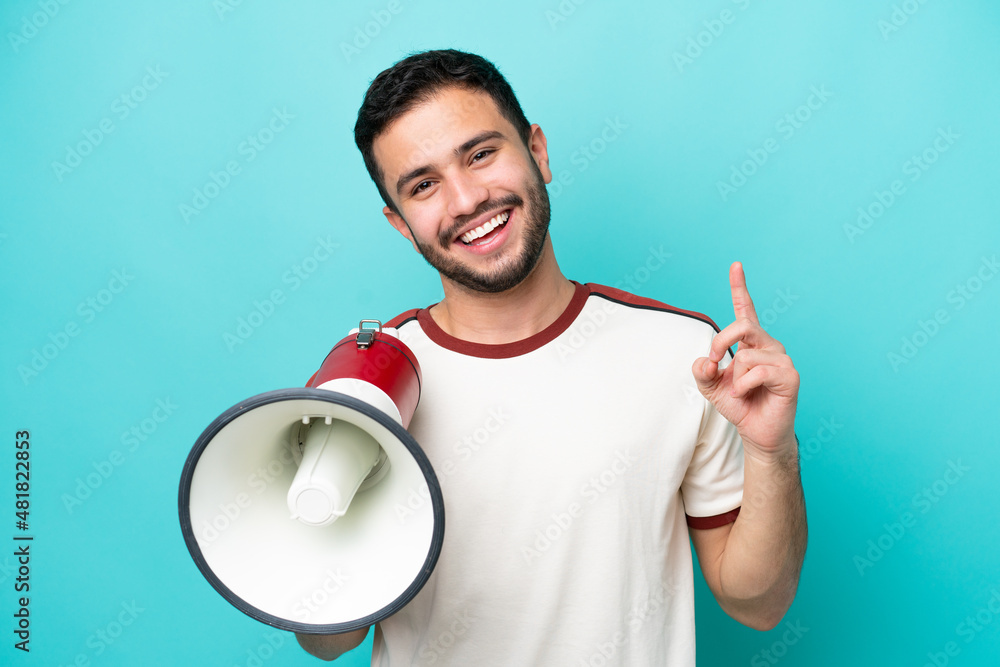 Young Brazilian man isolated on blue background holding a megaphone and pointing up a great idea Young Brazilian man isolated on blue background holding a megaphone and pointing up a great idea