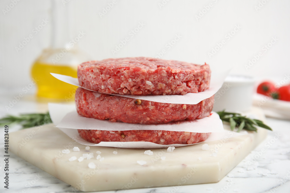 Raw hamburger patties with rosemary and salt on white marble table, closeup