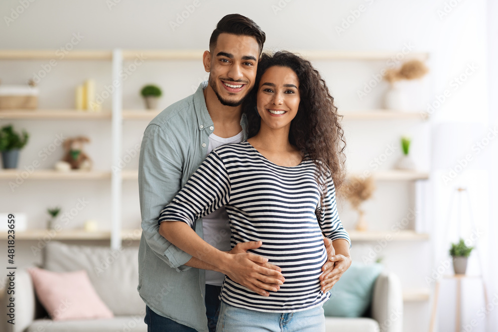 Fototapeta premium Happy middle-eastern man hugging his beautiful pregnant wife, posing together