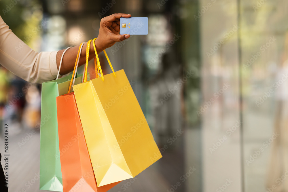 Unrecognizable black lady holding credit card and shopping bags